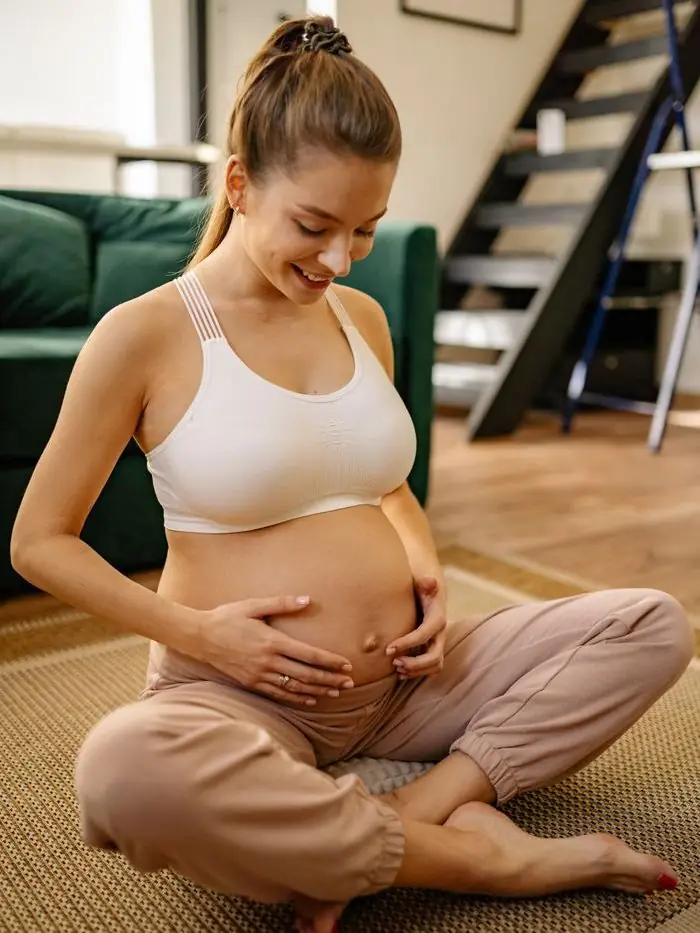 Grávida sentada no chão, com as mãos sobre a barriga