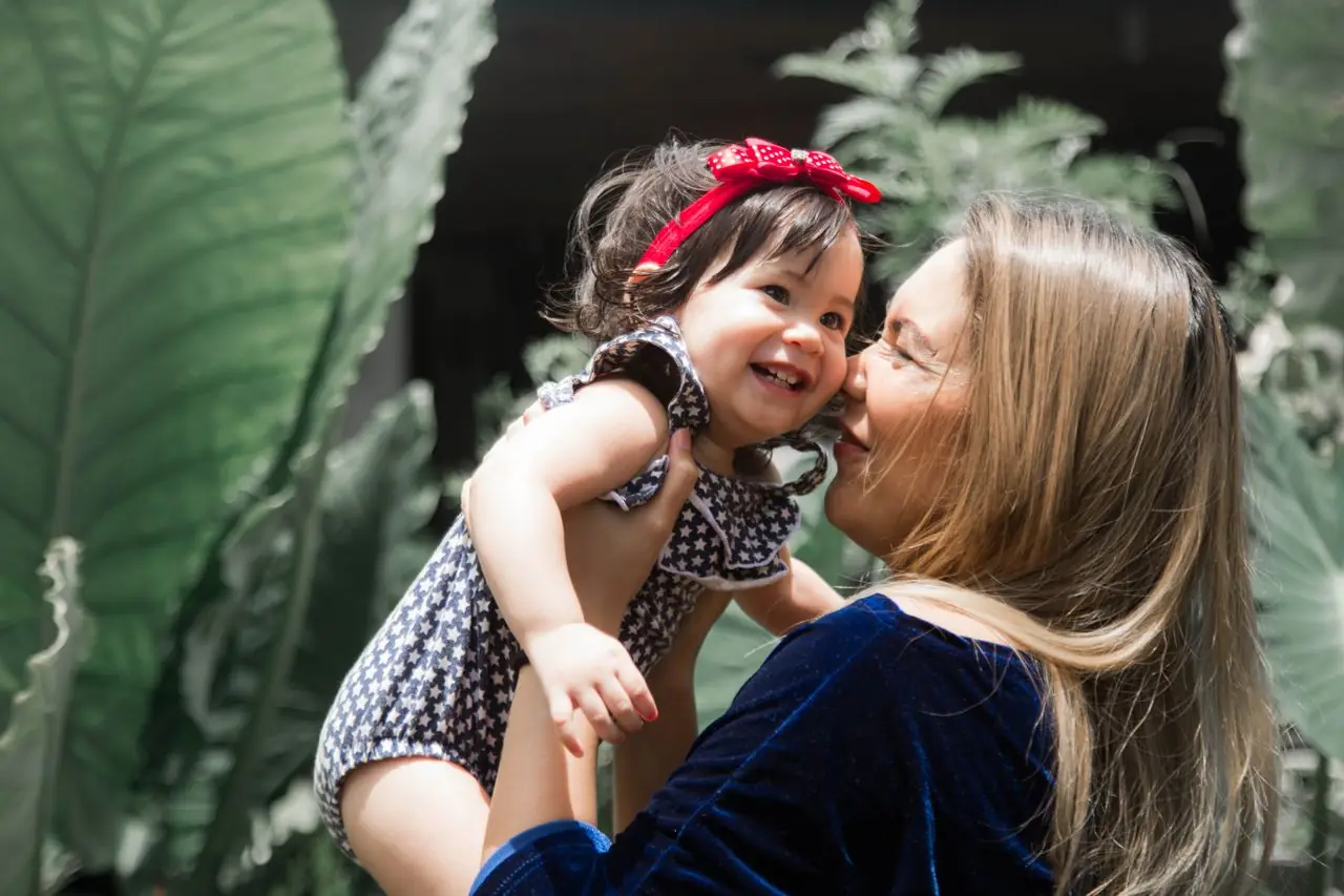 Mãe a segurar a filha ao colo, entre plantas